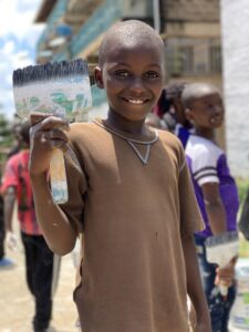 Children smiling in front of a community mural in Kitui