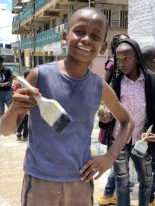 Children smiling in front of a community mural in Kitui