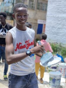 Children smiling in front of a community mural in Kitui